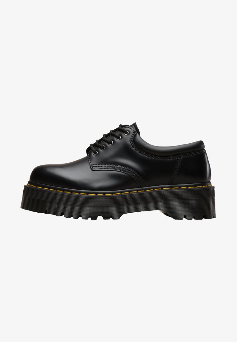 Scarpa nera in pelle con lacci, dotata di una soletta in gomma nera spessa e seghettata e cuciture gialle lungo il bordo, con una finitura liscia.