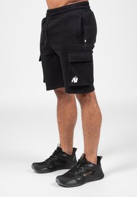 Black cargo shorts with an elastic waistband, side pockets, and a white gorilla graphic on the left leg, paired with black athletic shoes.