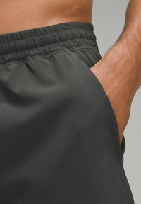 Shorts de sport noirs avec une taille élastique et une poche latérale, dotés d'un tissu lisse et d'une coupe décontractée.