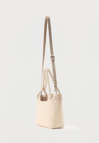 Μπεζ τσάντα tote με στριφτές λαβές από σχοινί και ρυθμιζόμενο δερμάτινο ιμάντα ώμου κρεμασμένη σε απλό φόντο.