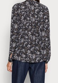 Musta kukkakuosinen pusero, jossa valkoisia ja keltaisia kukkia, pitkät hihat ja väljä istuvuus. Pyöreä pääntie ja sivuhalkiot.