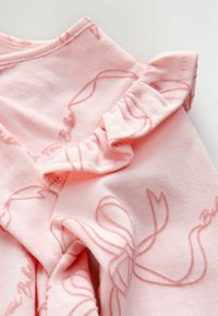 Tessuto rosa chiaro con dettagli di cuciture arricciate e testo ricamato in corsivo, che mostra la texture in primo piano e la costruzione del capo.