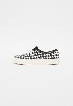 Sneaker w czarno-białym wzorze pied de poule, z teksturowanym płótnem, okrągłym noskiem, białym sznurowaniem i gumową podeszwą.
