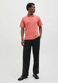 Korall színű pólóing gallérral és fehér díszítésekkel, fekete nadrággal párosítva. Az öltözet minimalista dizájnnal és sima textúrával rendelkezik.