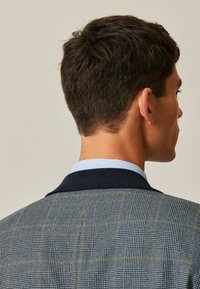 Blazer pour homme avec un motif à carreaux bleu et gris, col marine foncé et col intérieur bleu clair. Texture lisse, coupe ajustée.