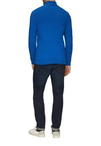 Blauer gestrickter Pullover mit Kragen, gerippten Bündchen und Saum. Kombiniert mit dunklen Jeans und weißen Sneakern. Einfaches Design, keine sichtbaren Muster.