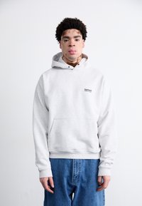 Grå hættetrøje med lomme foran og et lille logo på brystet, parret med løstsiddende blå denimjeans.