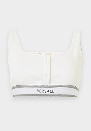 Hvid croppet tanktop med tre knapper foran og et gråt og hvidt elastikbånd med mærkenavnet "Versace" i sorte bogstaver.