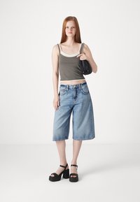Szara krótka koszulka tank top z kremowymi akcentami, niebieskie dżinsowe culottes i czarne platformowe sandały. Modelka trzyma małą czarną torebkę z łańcuszkiem.