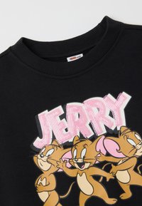 Felpa nera con un grafiche di topi dei cartoni animati e il nome "JERRY" in paillettes rosa. Collo tondo e polsini a coste.