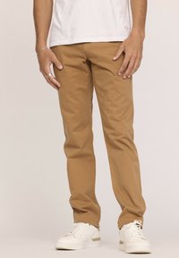 Chino beige clair avec une coupe droite, dotés de poches latérales et d'une texture lisse, associés à des baskets blanches.
