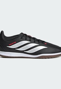 Μαύρο εσωτερικό παπούτσι ποδοσφαίρου Adidas Predator με λευκές ρίγες, κόκκινο λογότυπο, μαύρα κορδόνια και καφέ υφή σόλα, εμφανίζεται από το πλάι σε λευκό φόντο.