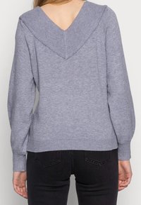 Light gray sweater with a V-back design, ribbed neckline, and cuffs. Soft texture, long sleeves, and fitted hem. Paired with dark jeans.