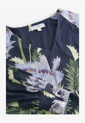 Marinebluse mit floralem Muster, V-Ausschnitt, gerafftem Ärmel und Knopfmanschette. Das Design zeigt lila Blumen und grüne Blätter auf glattem Stoff.