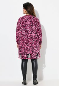 Langer pinkfarbener Leopard-Print Cardigan mit langen Ärmeln, der einen eingeschnittenen Saum aufweist, kombiniert mit schwarzen Leggings und verziert mit besetzten Stiefeletten.