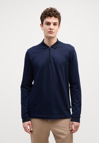 Polo de manga longa azul marinho com um padrão texturizado, colarinho com fecho de correr e punhos. Feito de um tecido suave, apresenta um corte ajustado.