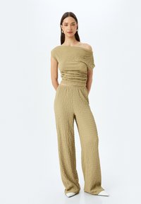 Licht olijfgroen twee-delig outfit met een textuur, geraffineerde top en broek met brede pijpen. Glad materiaal met een licht gekreukt patroon en een off-shoulder ontwerp.