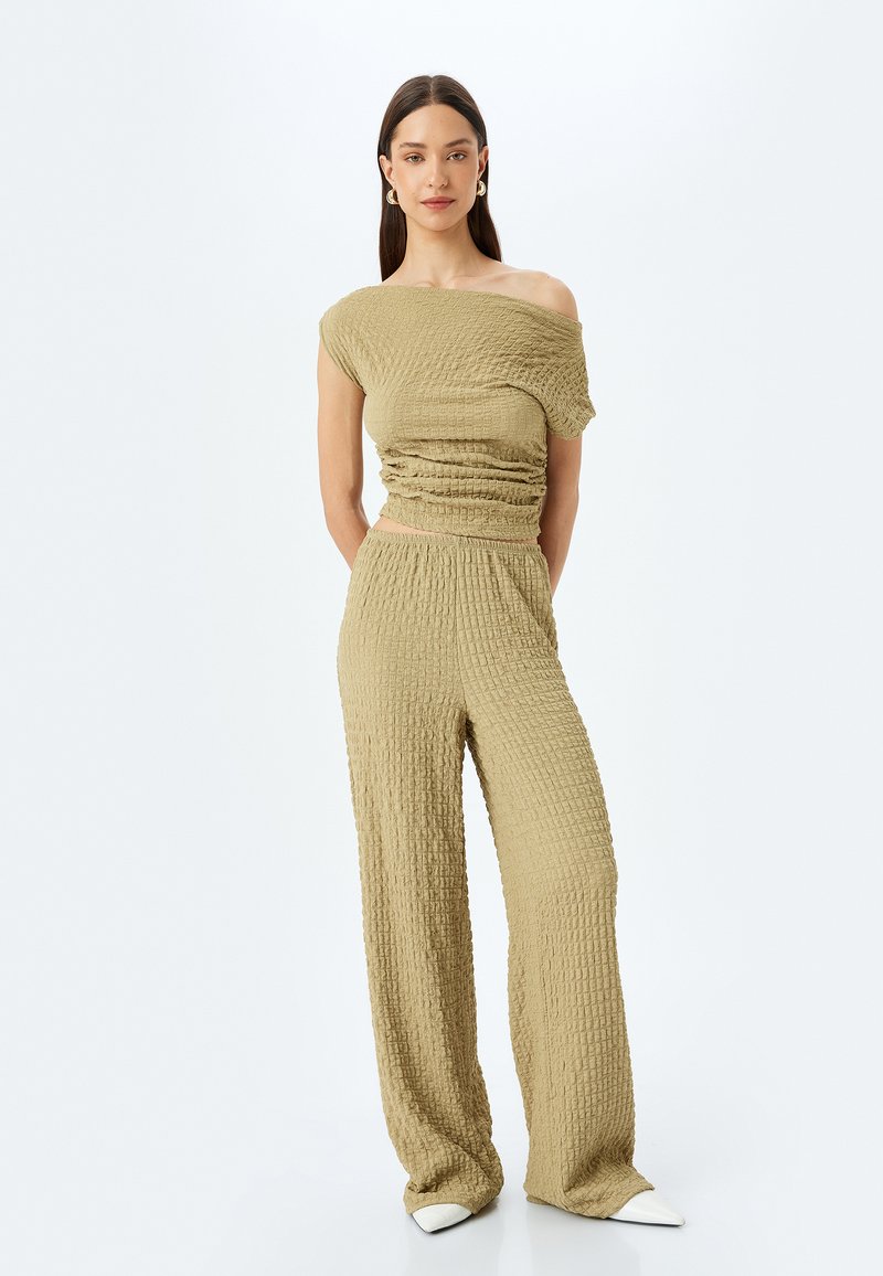 Licht olijfgroen twee-delig outfit met een textuur, geraffineerde top en broek met brede pijpen. Glad materiaal met een licht gekreukt patroon en een off-shoulder ontwerp.