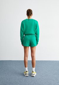 Zelená bavlněná mikina a šortky s volným střihem, s elastickým pasem. Kombinováno s teniskami a bílými ponožkami.