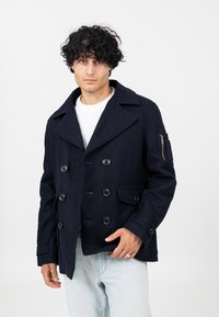 Granatowy wełniany płaszcz typu peacoat z podwójnym zapięciem, bocznymi kieszeniami i kieszenią na suwak na rękawie. Teksturowana tkanina z dopasowanym krojem.