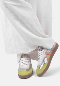 Sneaker multicolori con una combinazione di suede verde lime, materiale sintetico argentato e dettagli rosa; suola in gomma marrone; lacci bianchi.