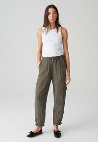 Olijfgroene lichte cargobroek met elastische boorden en een trekkoord in de taille, gecombineerd met een aansluitend wit tanktop en zwarte flats.
