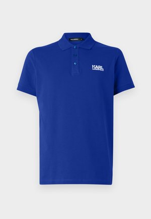 Mėlynas polo marškinėliai pagaminti iš medvilnės, su klasikiniais atvartais, trimis mygtukais ir baltu logotipu kairėje krūtinės pusėje. Trumpomis rankovėmis, lygiu paviršiumi.
