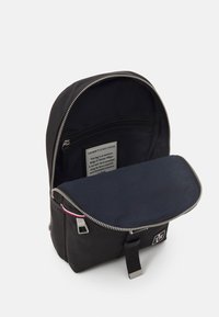 Zaino in nylon nero con forma arrotondata, cerniera argento e tasca frontale. Interno blu con etichetta che dettaglia le informazioni sul prodotto.