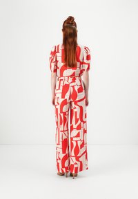 Combinaison à motifs rouge et blanc avec des manches bouffantes, taille cintrée et pantalons évasés, présentant des formes abstraites et une finition texturée.