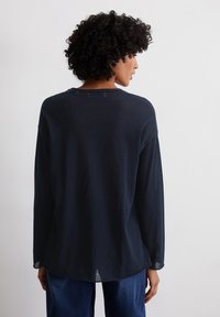 Camicia a maniche lunghe blu navy con un taglio rilassato e orlo arrotondato. Realizzata in tessuto leggero e leggermente strutturato. Presenta un semplice collo a girocollo.