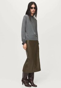 Gray knitted sweater with long sleeves, paired with a dark green leather skirt and knee-high brown heeled boots. Styled with dark sunglasses.