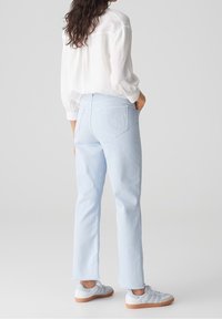 Jean droit bleu clair en denim, porté avec une chemise blanche à manches longues texturée et des baskets blanches à semelle en gomme.