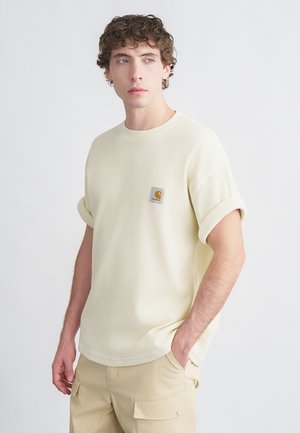 T-shirt gialla chiaro a coste con maniche arrotolate, scollo rotondo e una piccola toppa con logo quadrato sul petto. Indossata con pantaloni cargo beige.