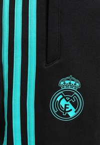 Schwarze Sportshorts mit türkisfarbenen Streifen und einem gestickten Logo mit einer Krone und Initialen auf der linken Seite. Strukturierten Stoff.
