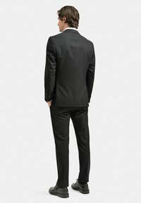 Svart kostym med slim fit-design, enfärgat kavaj och byxor med rak front. Slät tyg, minimalistisk stil, parat med svarta skor.