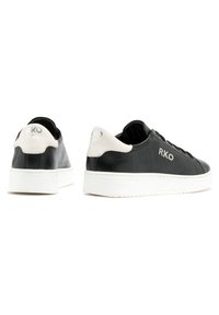 Baskets en cuir noir avec semelles blanches, présentant un accent blanc au talon et le logo "RKO" embossé sur le côté et à l'arrière.