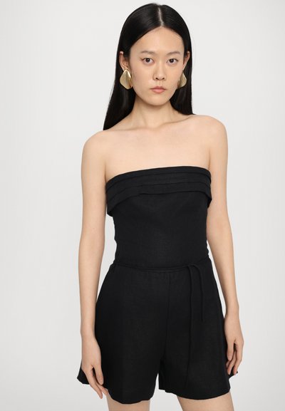 Melna strapless rompa ar daudzslāņu detaļām augšā, iešūta jostasvieta un brīvi šorti. Gluda auduma un brīva piegriezuma. Zelta izteiksmīgas auskaru stiprinājumi.