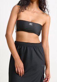 Černý bandeau top s bílým logem Adidas; hladká látka a přiléhavý střih. Kombinováno s černými šortkami se zipy a logem.