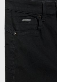 Jeans de mezclilla negra con un bolsillo frontal, etiqueta de marca plateada y costuras en contraste. Diseñados con un corte recto y un minimalismo en los detalles.
