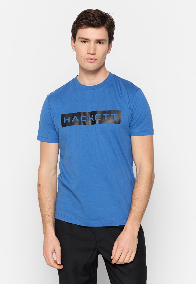 T-shirt en coton bleu à manches courtes, col rond, avec un logo rectangulaire noir portant le mot "HACKETT" en texte blanc sur la poitrine.