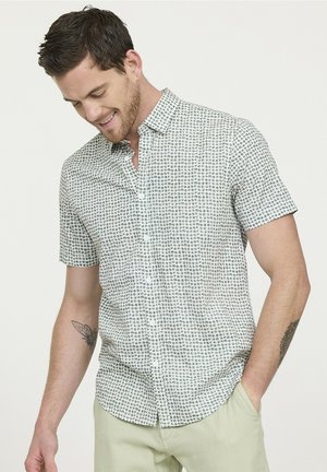 Chemise à manches courtes à boutons de couleur vert clair avec un motif géométrique. Le tissu a une texture lisse avec un éclat subtil. Boutons blancs visibles.