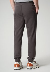 Pantaloni della tuta grigi con polsini elasticizzati e tasche laterali, realizzati in un tessuto morbido. Abbinati a scarpe da ginnastica bianche e arancioni.