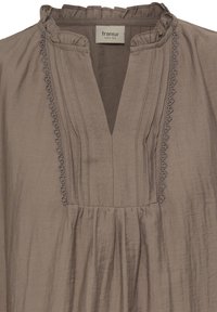 Blouse taupe avec col à volants, encolure en V, plis verticaux et délicate finition brodée le long de l'ouverture sur la poitrine.