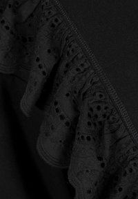 Czarna bluzka z falbaną z koronkowym wykończeniem i detalami w oczka. Tekstura materiału jest gładka, z miękkim wykończeniem wokół dekoltu.