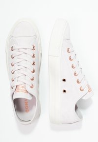 Baskets en daim gris clair avec œillets en or rose, semelles en caoutchouc blanc et coutures texturées contrastées ; étiquette logo sur la languette.