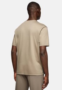 Beige cotton t-shirt with short sleeves. Simple design, rounded neckline, and smooth texture. Seen from the back, with a straight cut.