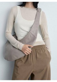 Sac d'épaule en cuir gris avec une forme arrondie et une bandoulière ajustable. Texture lisse avec un minimum de ferrures et des éléments de design simples.