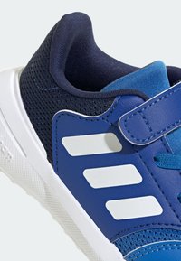 Niebieskie i granatowe sneakersy z białą podeszwą, trzema białymi paskami po bokach, z siateczkowego materiału oraz z zapięciem na rzep.