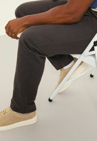 Dark grey, slim-fit pants made of cotton blend, featuring side seams and a smooth texture. Beige suede sneakers with white soles.