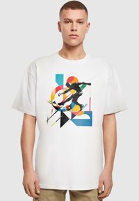 Hvid t-shirt med en sort silhuet af en skater, fremhævet med farverige geometriske former i orange, blå og sort.